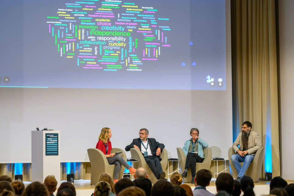 During the panel discussion on "Academic Freedom in a Changing International Landscape," moderator Sophie Stigler and panelists Walter Rosenthal, Katrin Kinzelbach, and Stefan Klumpp are seated on stage. In the background, a Mentimeter poll is displayed, showing a word cloud with words like "freedom," "creativity," and "independence."