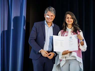 Two people on a stage, one person holding a certificate in their hand
