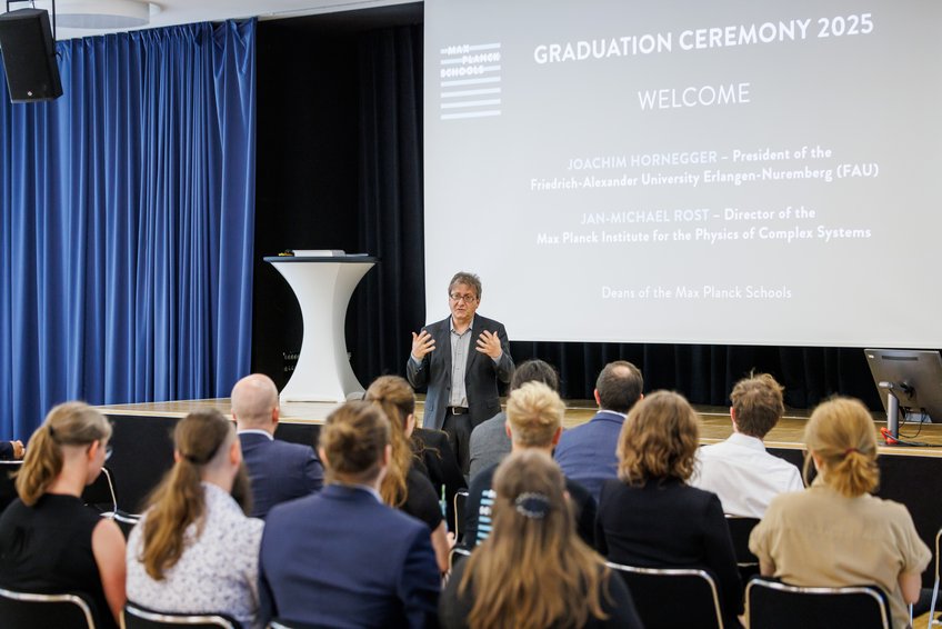 Prof. Jan-Michael Rost, einer der beiden Max Planck Schools Deans, eröffnete die Veranstaltung auf dem Bildungscampus in Heilbronn Zuhörer in einem Auditorium bei einer Abschlusszeremonie, auf der Leinwand Begrüßung durch Joachim Hornegger und Jan-Michael Rost.