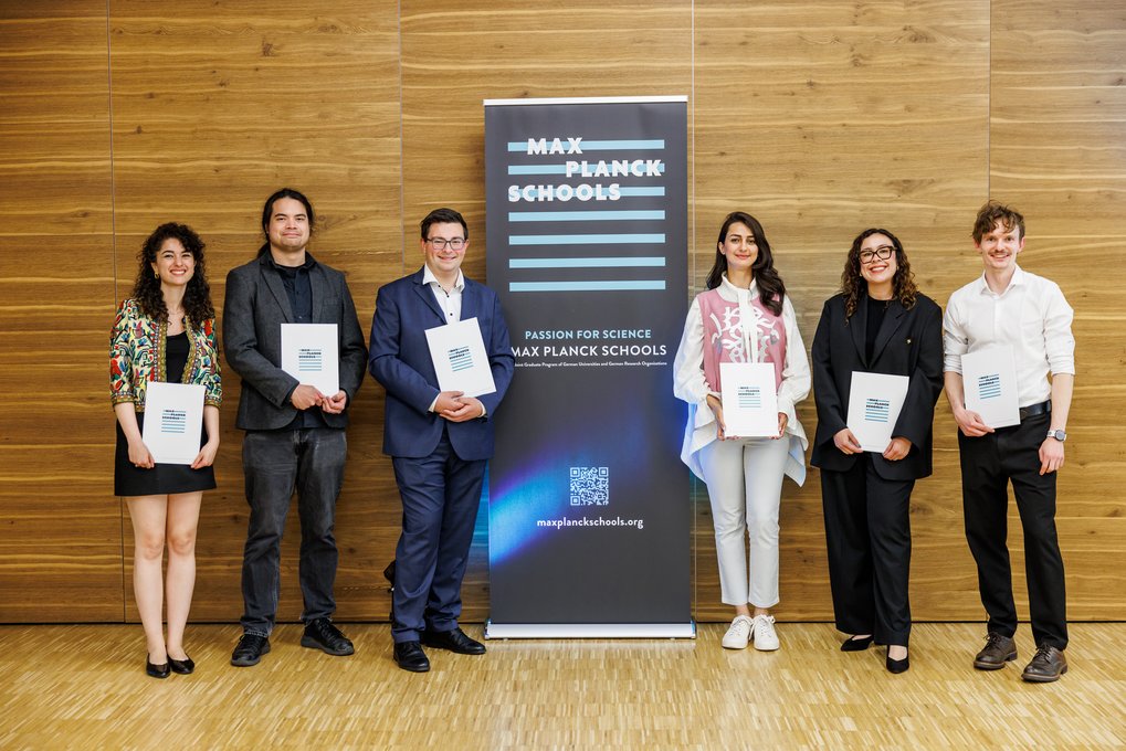 Six individuals stand beside a Max Planck Schools banner, holding certificates.