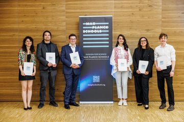 Six individuals stand beside a Max Planck Schools banner, holding certificates.