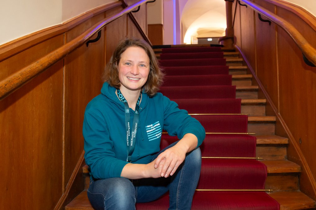 Eine Person trägt einen blauen Hoodie und sitzt auf einer breiten Holztreppe, die mit einem roten Teppich bedeckt ist.