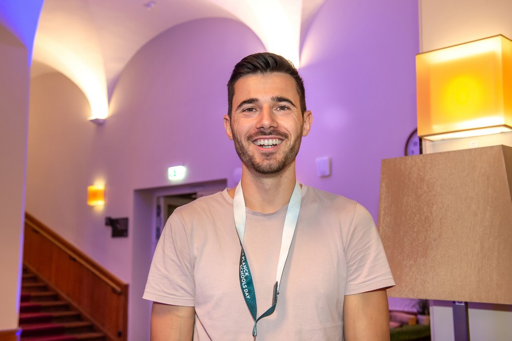 Person trägt ein weißes Lanyard, steht vor einem beleuchteten Raum mit gebogenen Wänden.