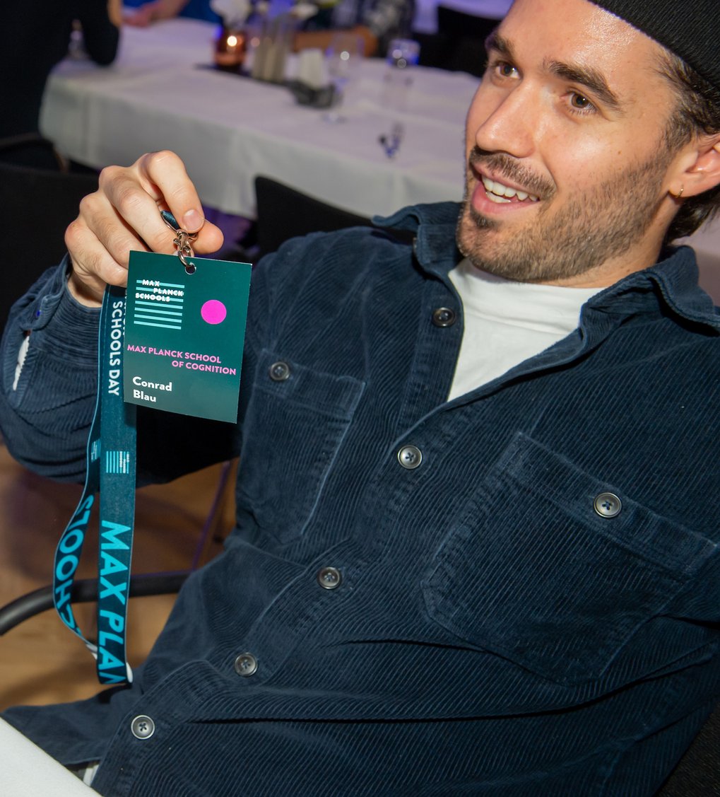 Ein blaues Namensschild mit der Aufschrift "Max Planck School of Cognition" und dem Namen "Conrad Blau" wird von einer Person gehalten.
