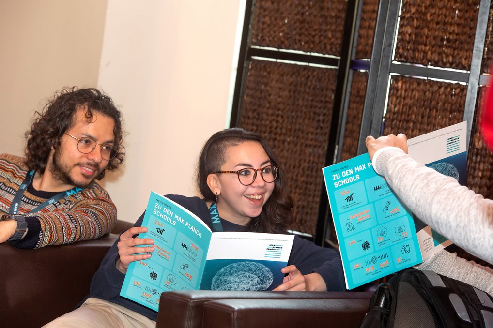 Zwei Personen lesen Informationsbroschüren über Max Planck Schools in einem Raum.