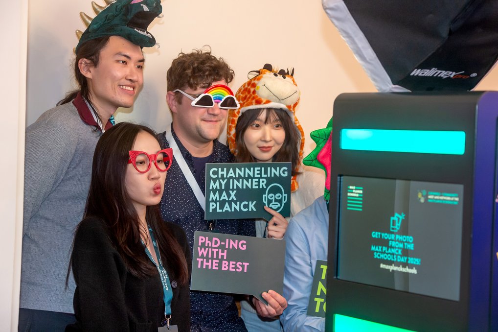 Gruppenveranstaltung mit ausgefallenen Hüten und Brillen, Fotobox im Vordergrund, Display zeigt Max Planck Schools Day 2022.