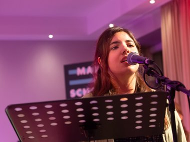 A music stand with sheet music and a microphone in a room illuminated by purple lighting, with a partially visible sign in the background.